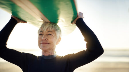 Senior woman carrying a surfboard on her head at the beach